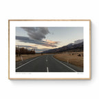A serene landscape photograph of a road in New Zealand with Aoraki/Mt Cook in the background under a twilight sky with dynamic cloud formations.