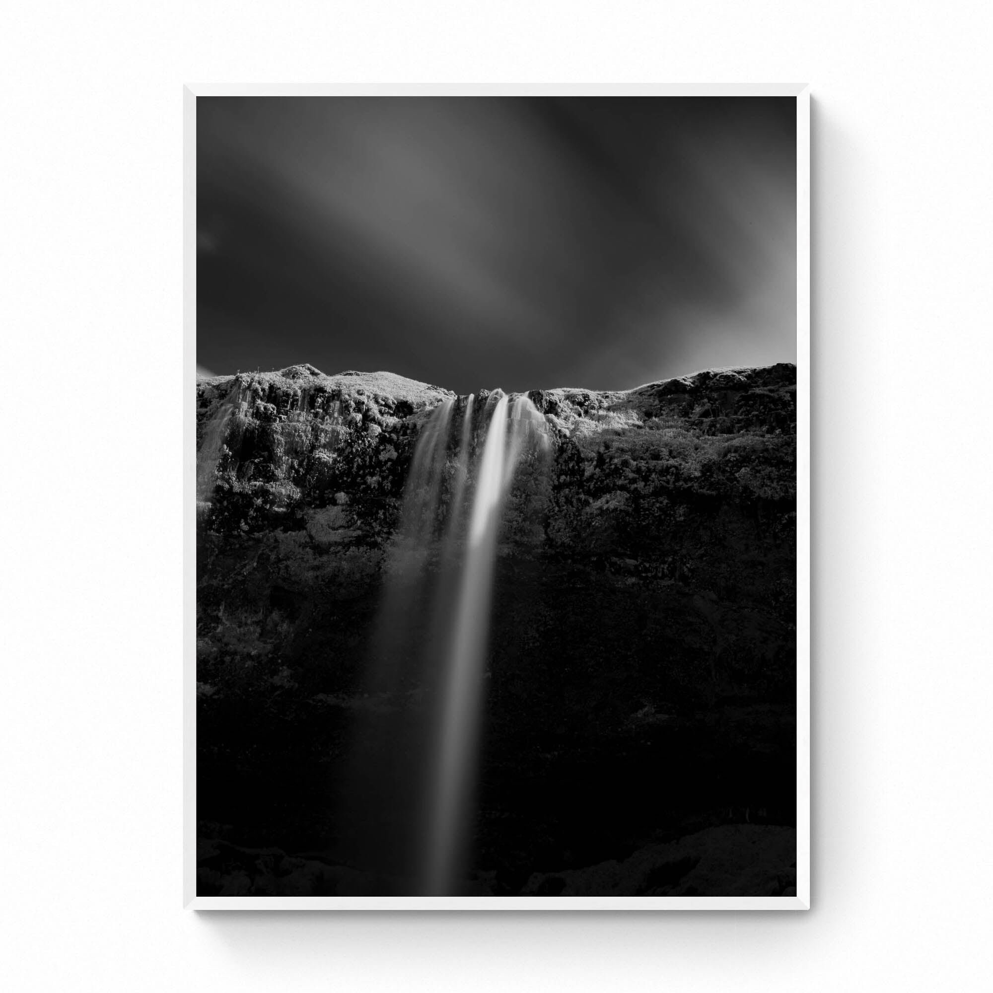 A black and white long-exposure photograph of Seljalandsfoss waterfall in Iceland, showing smooth water streams against a dark, textured cliff.