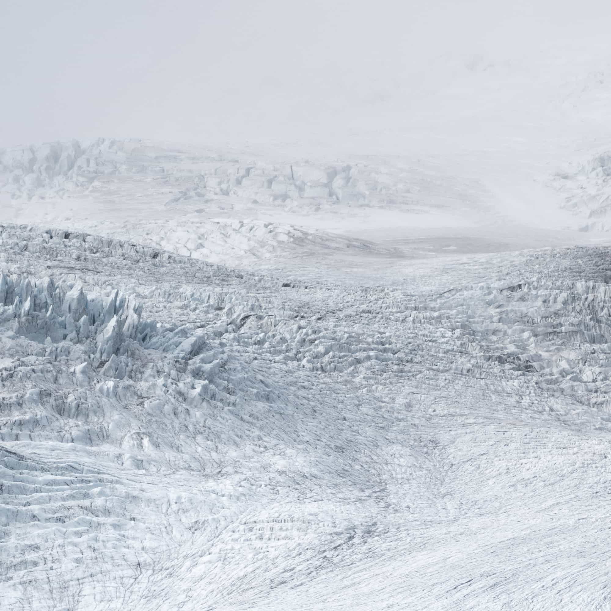 A monochromatic view of an expansive glacier in Iceland, showing textured ice formations under a subtle gray sky.