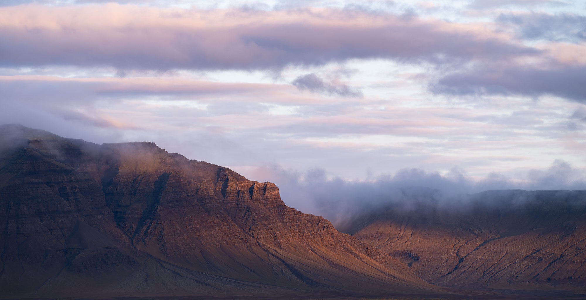 Late evening light bathes the Snæfellsnes Peninsula mountains in a warm glow with pink-tinged clouds above in Iceland.