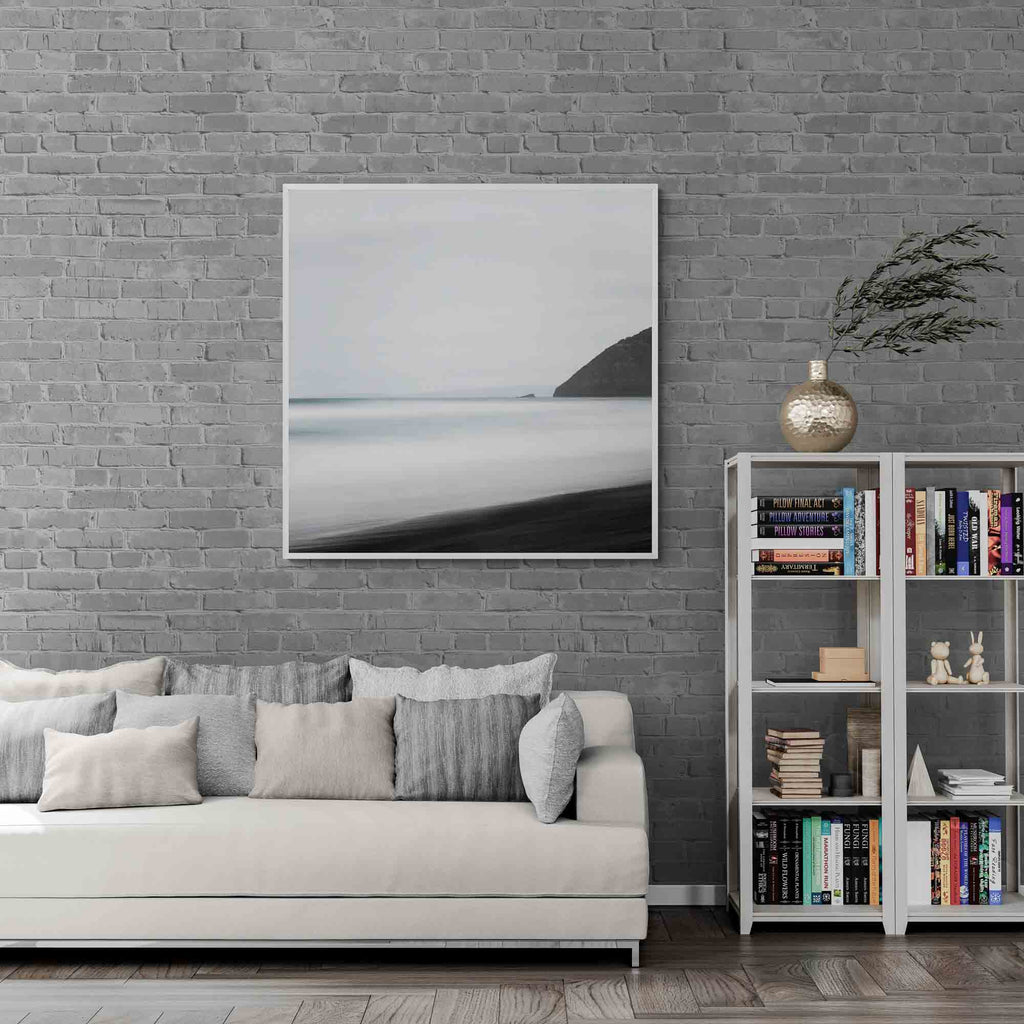 A minimalist long exposure photo of the calm sea meeting the dark sands of St. Clair's Beach in New Zealand, with a headland silhouette on the right.