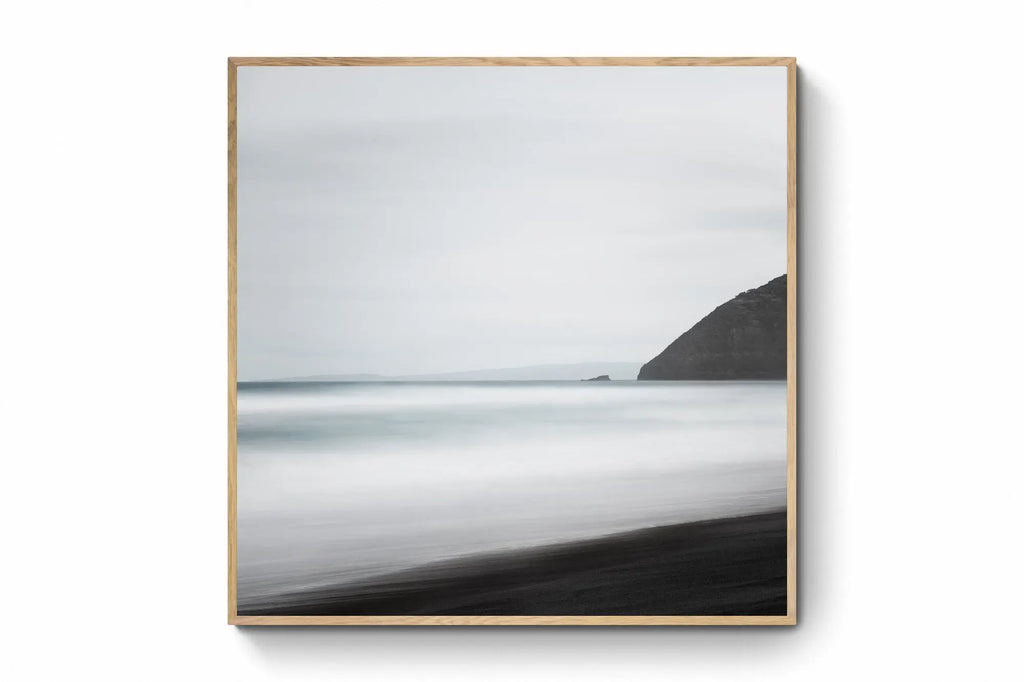 A minimalist long exposure photo of the calm sea meeting the dark sands of St. Clair's Beach in New Zealand, with a headland silhouette on the right.