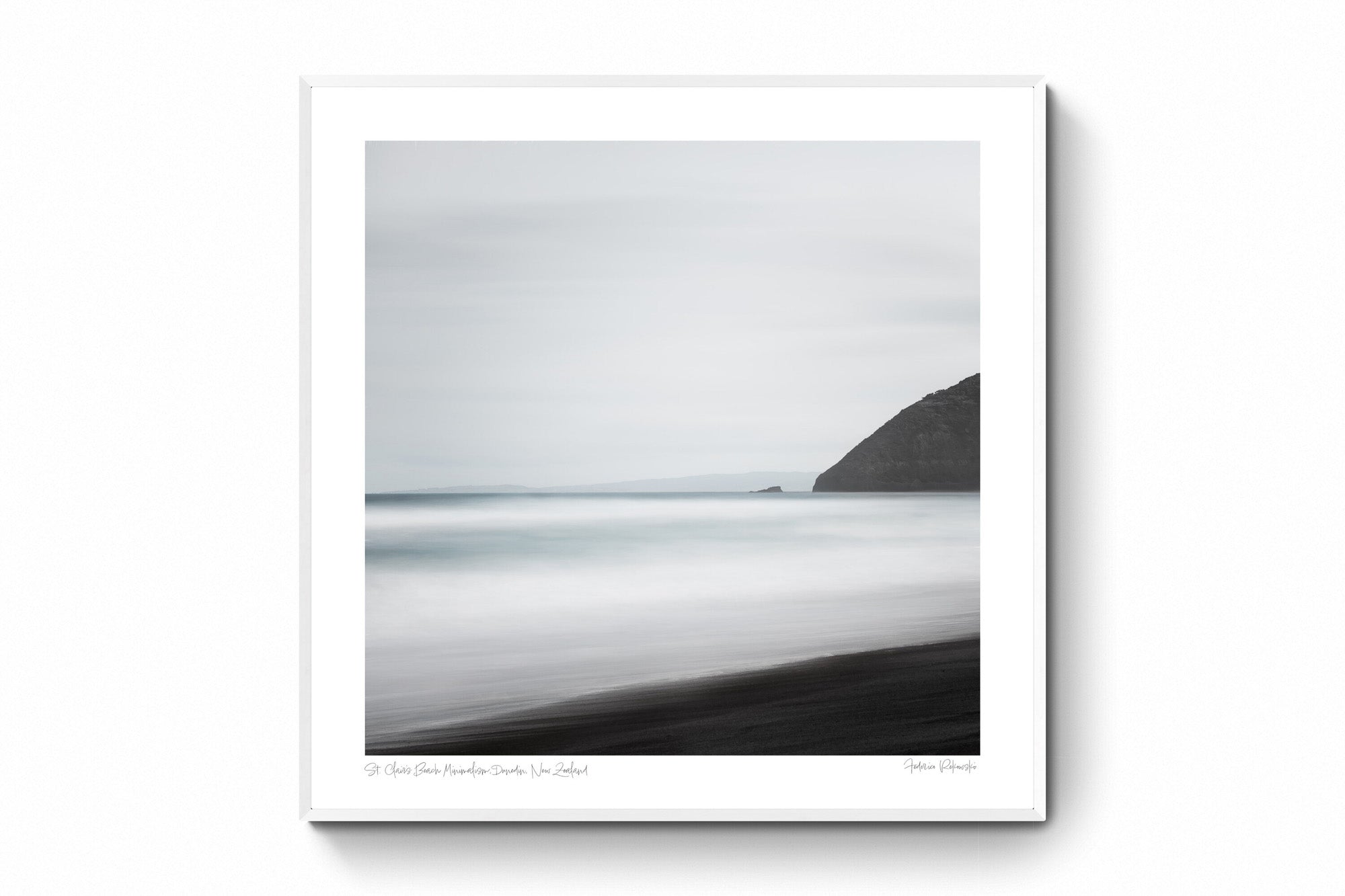 A minimalist long exposure photo of the calm sea meeting the dark sands of St. Clair's Beach in New Zealand, with a headland silhouette on the right.