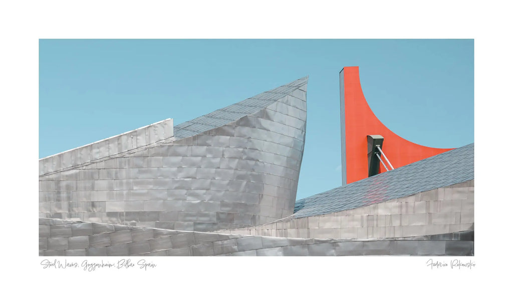 The Guggenheim Museum Bilbao, with its metallic curves contrasted by a bright red architectural feature against a clear blue sky.