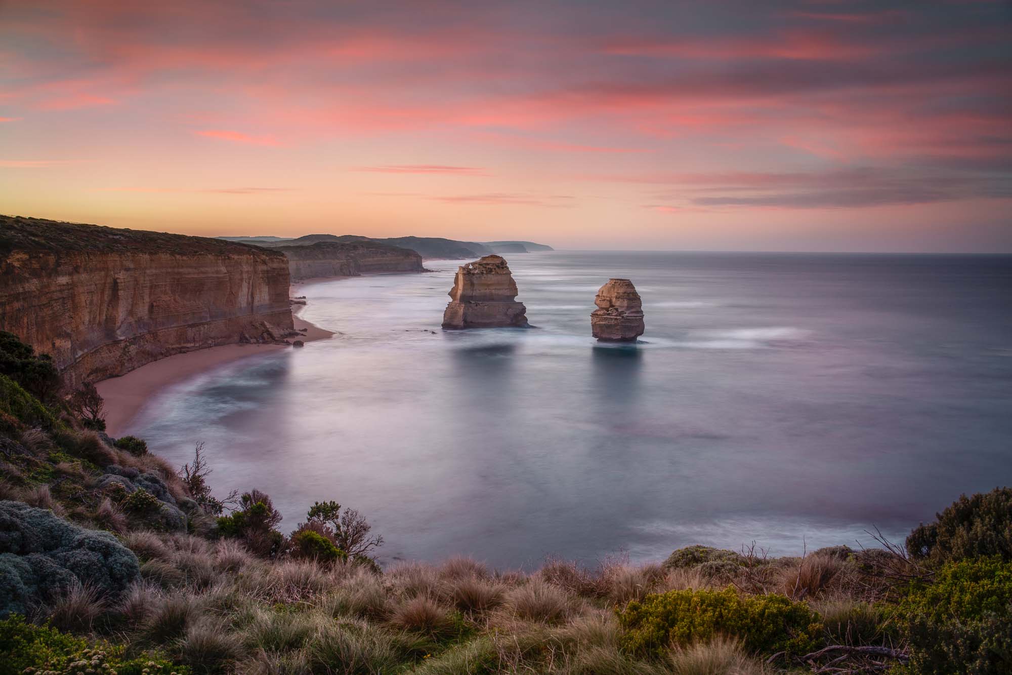 Sunset at The Twelve Apostles, with smooth seas and pastel skies highlighting the limestone formations off Australia's coast.