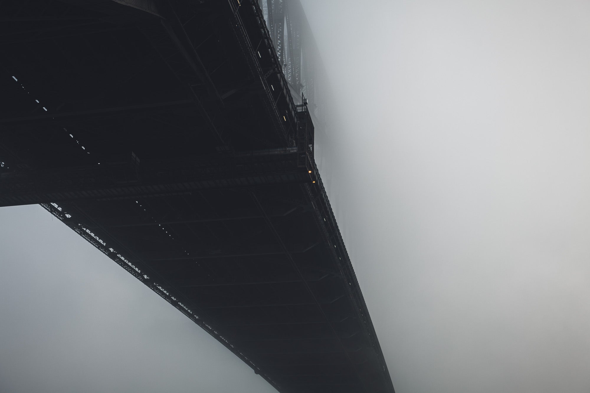 The Sydney Harbour Bridge partially obscured by fog, with its arch and lights fading into the white mist.