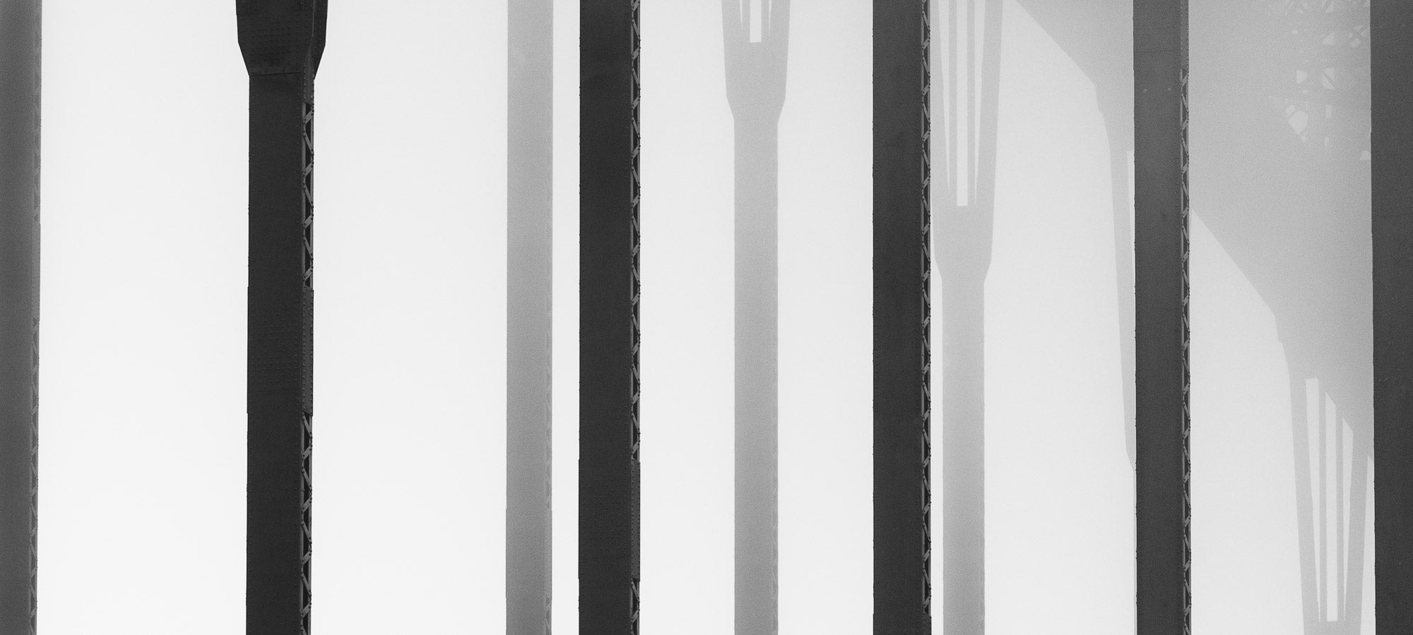 Black and white close-up of the vertical steel stanchions of Sydney Harbour Bridge, displaying a play of light and shadows.