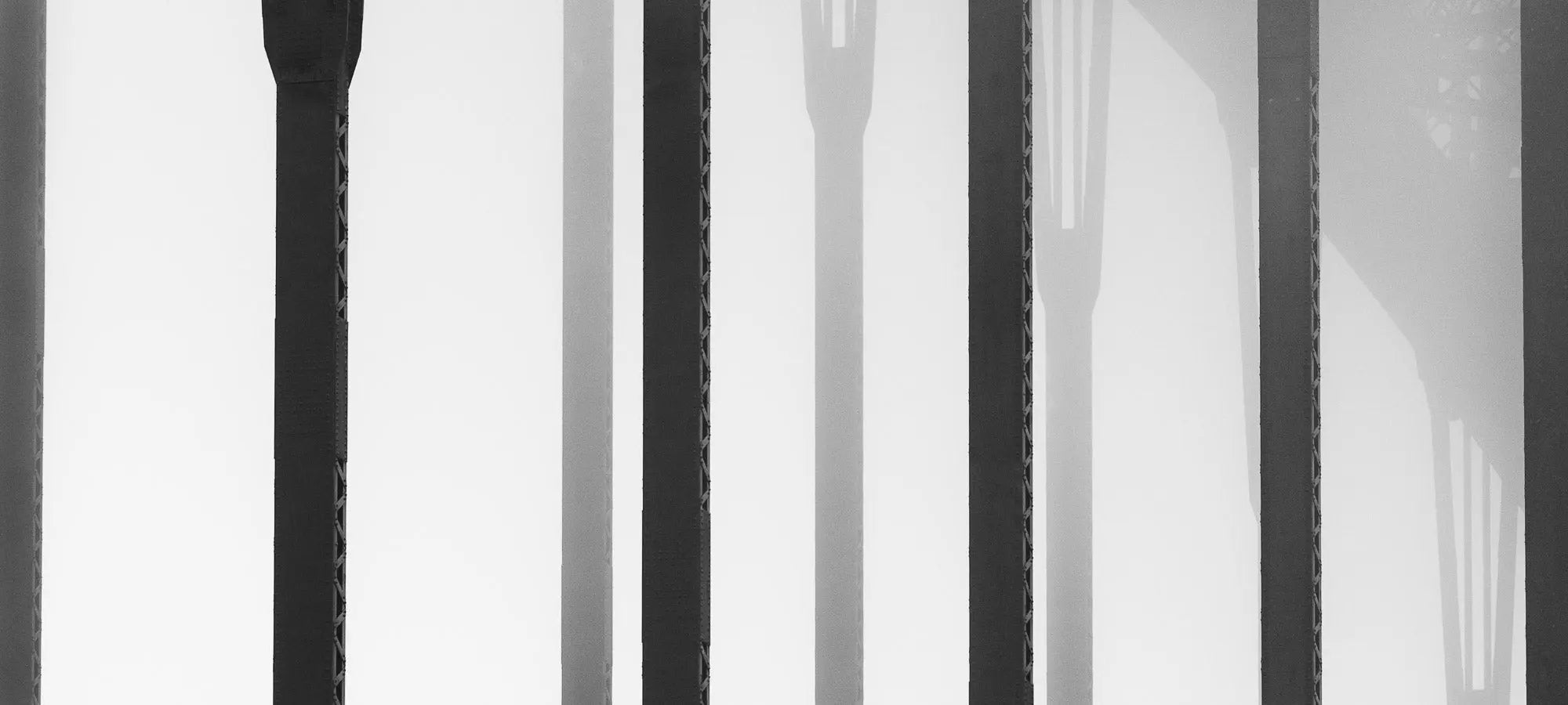 Black and white close-up of the vertical steel stanchions of Sydney Harbour Bridge, displaying a play of light and shadows.