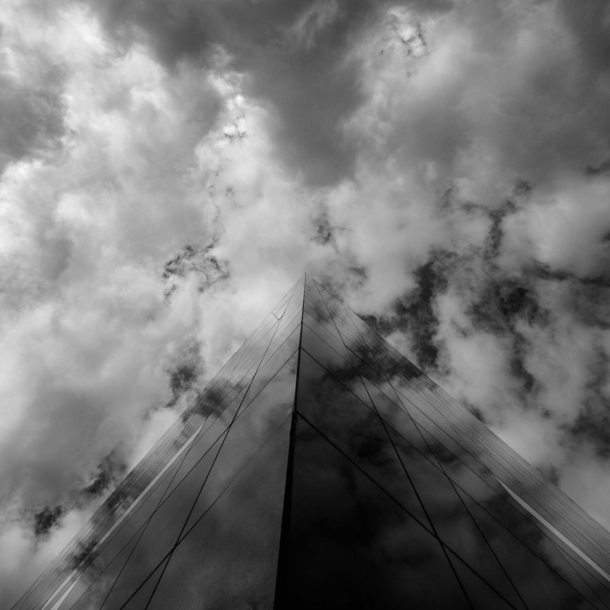 "Black and white photo of the BLOX building in Copenhagen, with its reflective glass facade reaching into a dramatic sky."