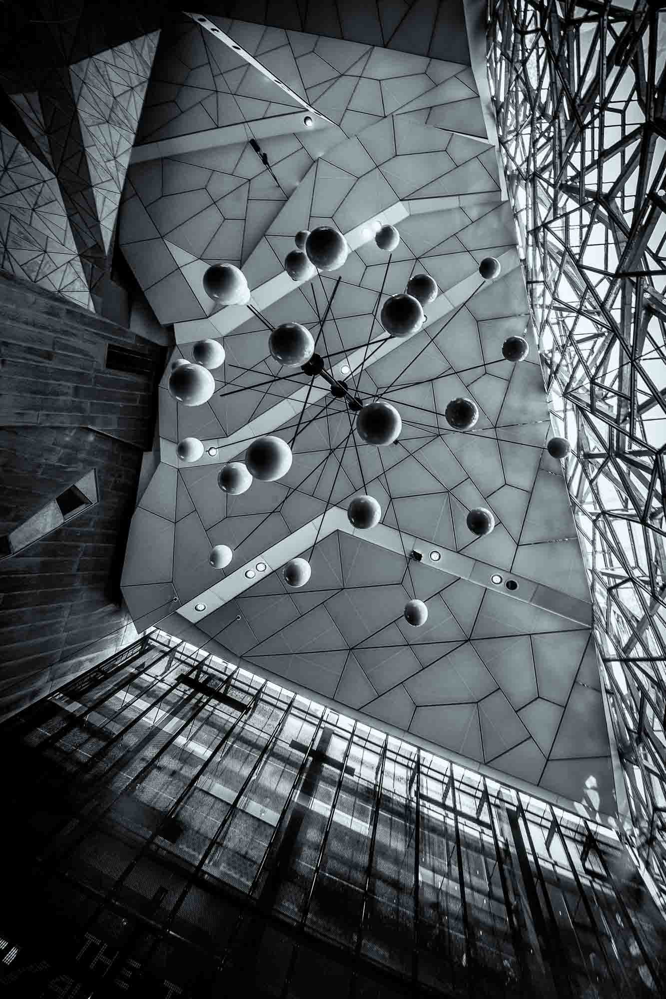 Black and white photo of the abstract geometric ceiling at Federation Square in Melbourne, with spherical elements hanging against the angular design.