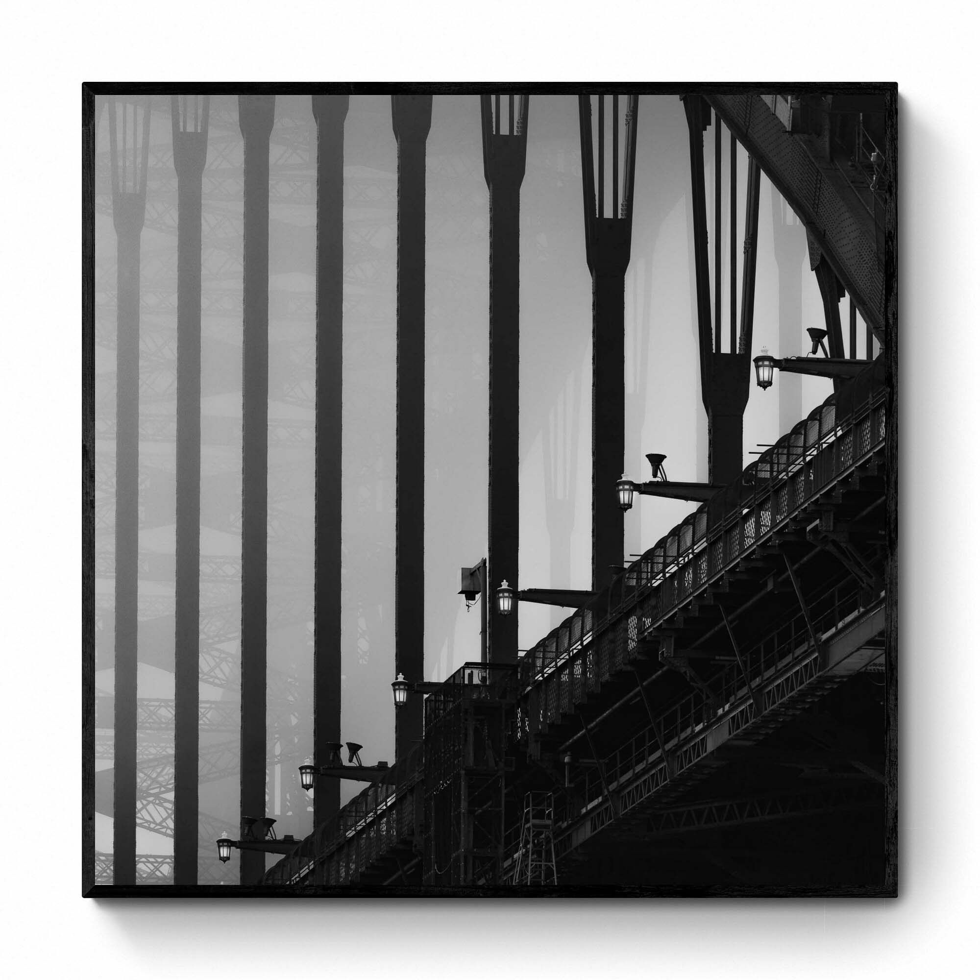 Monochrome image of Sydney Harbour Bridge, showing the contrast of the stark, strong lines of its arches and street lamps against the light sky.
