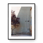 A single tree with autumn-colored leaves beside a large, plain wall with small openings, in Zaragoza, Spain.