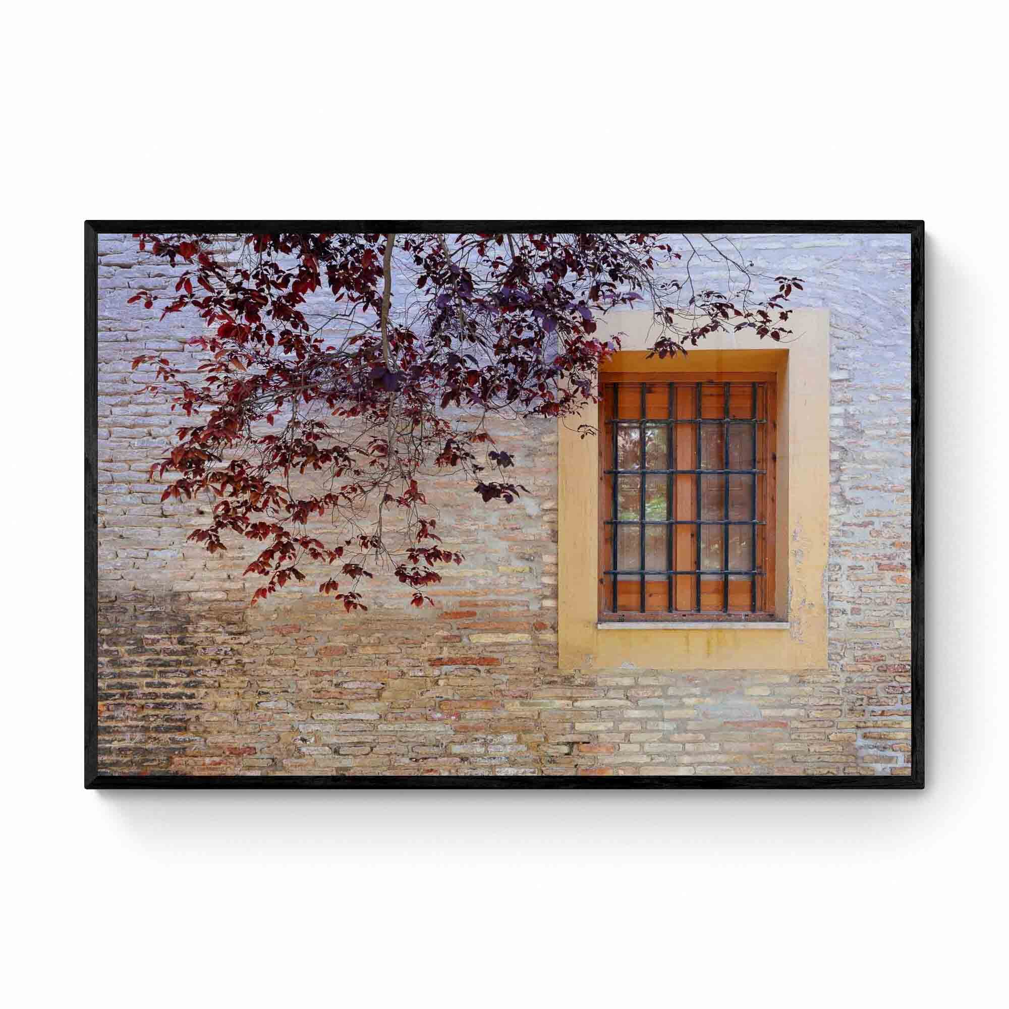 A rustic window with a yellow frame set in an old brick wall, adorned by autumn leaves, in Zaragoza, Spain.