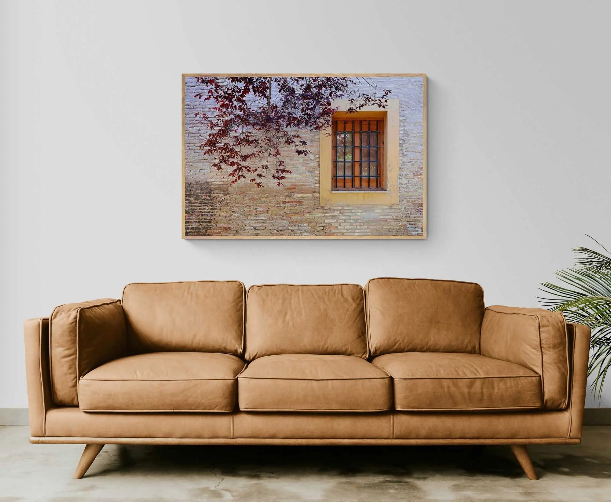 A rustic window with a yellow frame set in an old brick wall, adorned by autumn leaves, in Zaragoza, Spain.